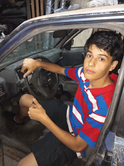 a young boy in a red white and blue shirt is sitting in a car