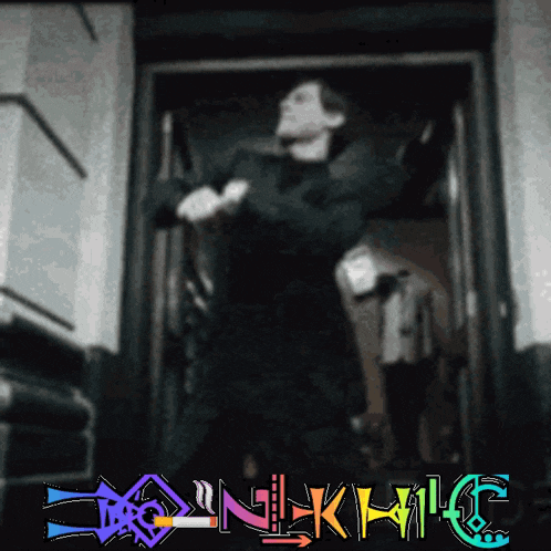 a man is standing in a doorway with a colorful sign above him that says ' nkmic ' on it