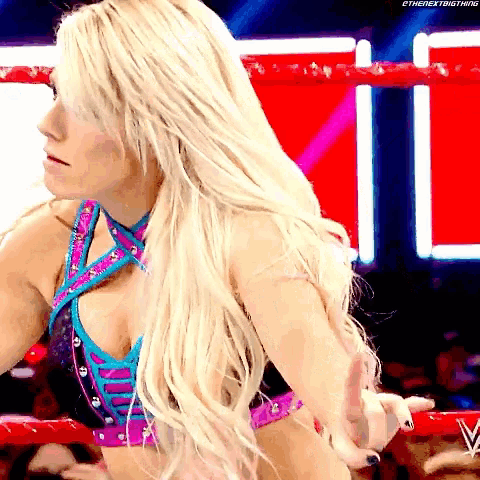 a blonde woman is standing in a wrestling ring with her hands in the air .