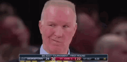 a man in a suit and tie stands in front of a scoreboard that says big east tournament first round