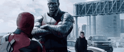 a giant statue of colossus is standing next to a man in a red hoodie .