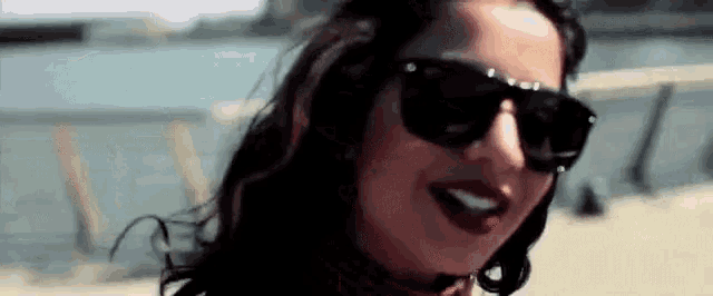 a woman wearing sunglasses and red lipstick is smiling and looking at the camera .