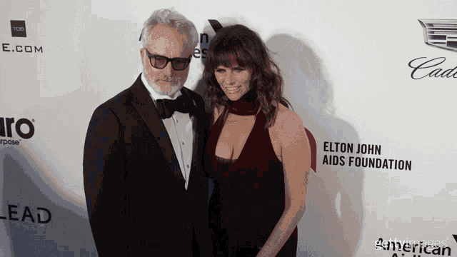 a man and a woman pose on a red carpet with elton john aids foundation written on it