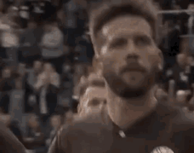 a man with a beard is screaming in front of a crowd of people in a stadium .