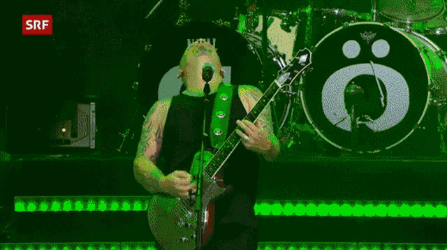 a man singing into a microphone while playing a guitar in front of a drum set with a srf logo in the background
