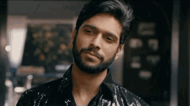 a man with a beard is wearing a black sequined shirt and smiling
