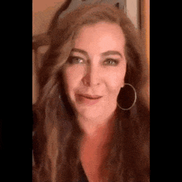 a woman with long brown hair and hoop earrings is smiling .