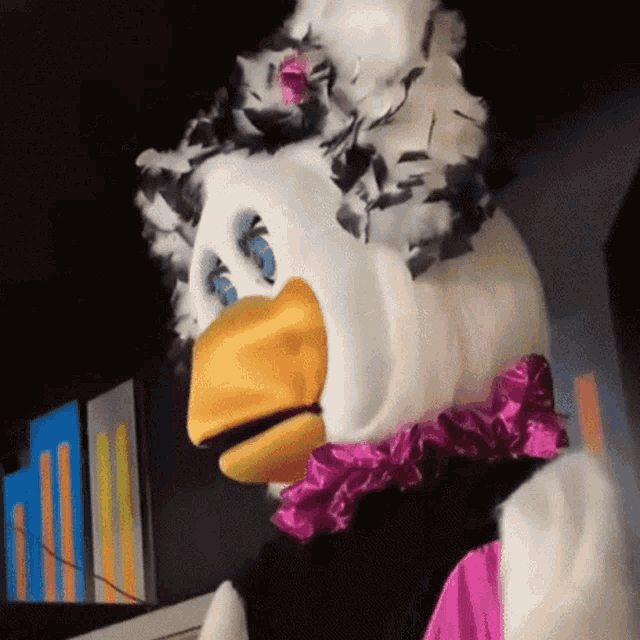 a mascot wearing a feathered headpiece and a pink bow tie