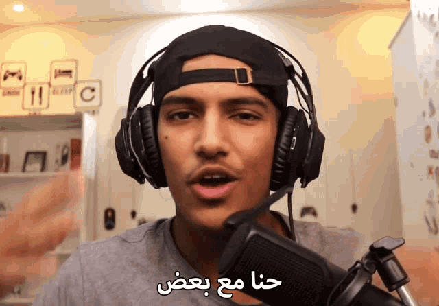 a man wearing headphones and a hat is talking into a microphone with arabic writing on it