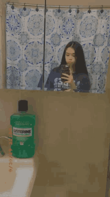 a woman is taking a picture of herself in a bathroom mirror next to a bottle of listerine .