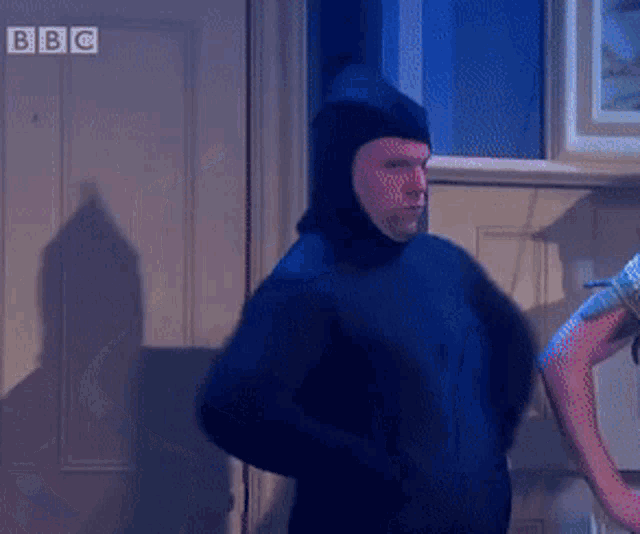 a man in a blue sweater is standing in front of a door with bbc written on it