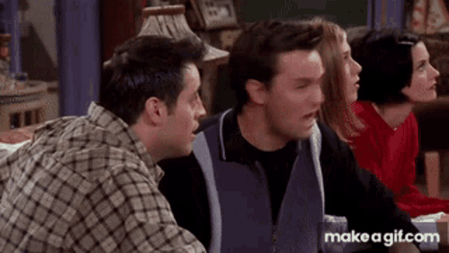 a group of people are sitting around a table and one of them is making a funny face .