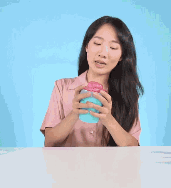 a woman in a pink shirt is holding a blue cup with a heart on it
