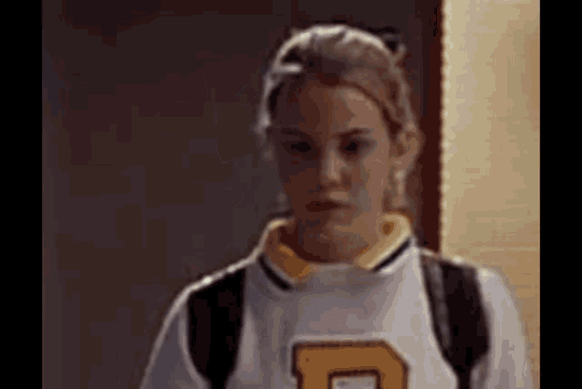 a woman wearing a cheerleader uniform with the letter d on it is standing in a hallway .