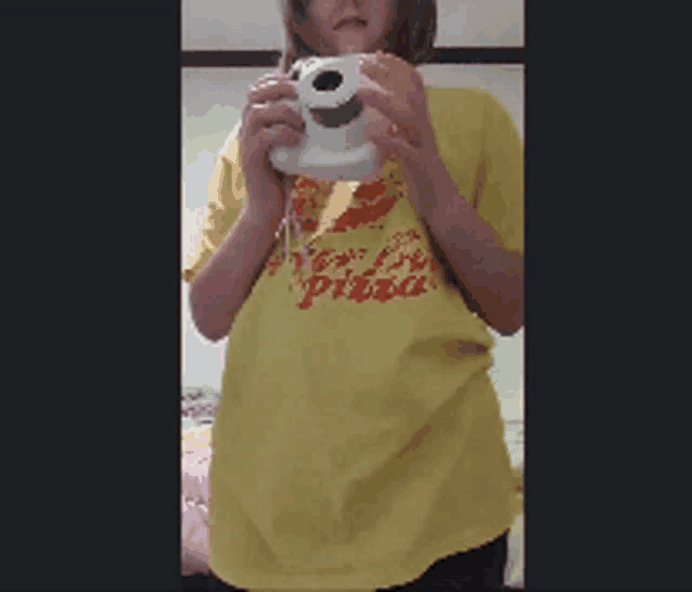 a woman wearing a yellow shirt that says pizza holds a camera