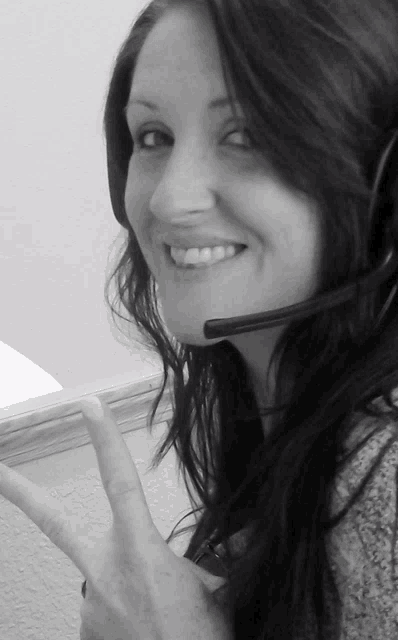 a woman wearing a headset smiles while giving a peace sign
