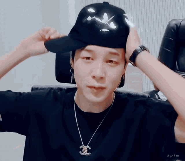 a man wearing a black hat and a necklace with a chanel pendant