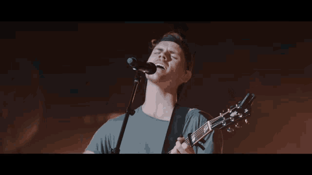 a man singing into a microphone while holding an acoustic guitar