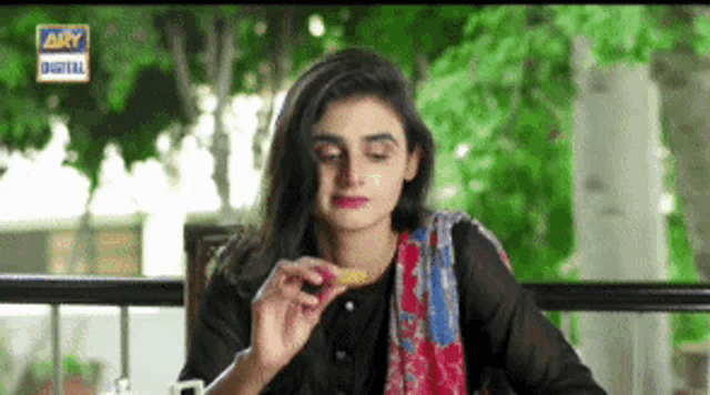 a woman is eating a piece of food while sitting at a table with a sign that says ary digital
