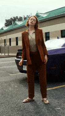 a woman in a brown suit stands in front of a purple car with a license plate that says nct