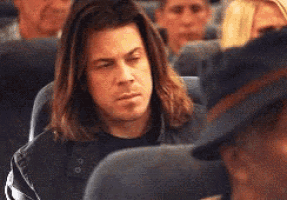 a man with long hair is sitting on a plane looking at his phone