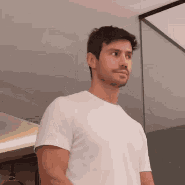 a man in a white t-shirt stands in front of a mirror