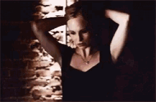 a woman in a black tank top is standing in front of a brick wall .