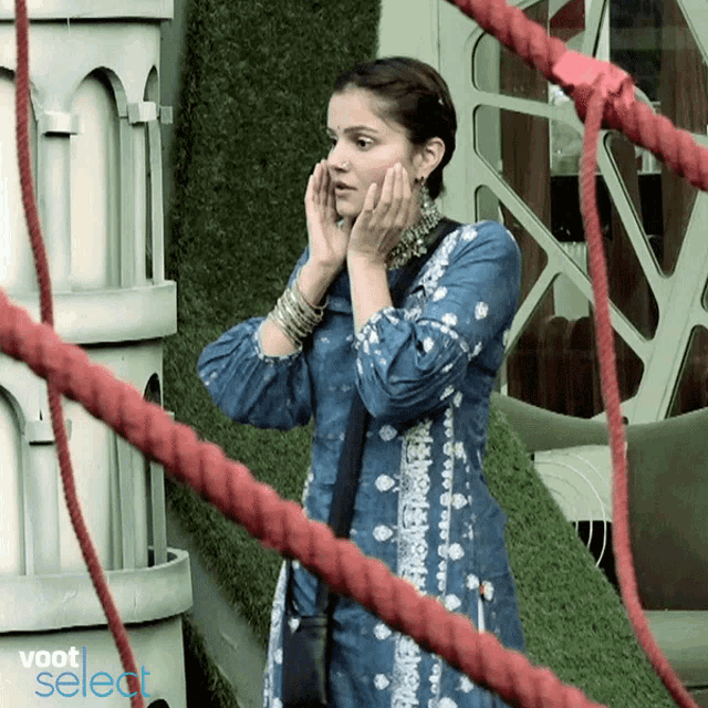 a woman in a blue dress stands in front of red ropes and a sign that says voot select on it