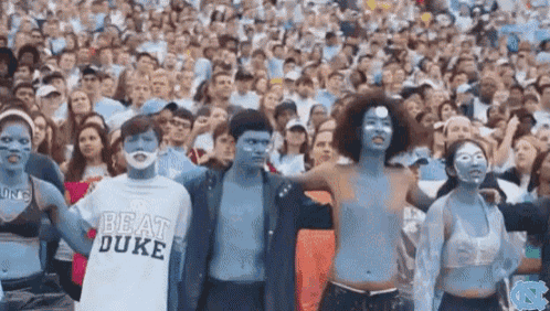 a crowd of people are standing in a stadium wearing blue paint on their faces and shirts that say beat duke .