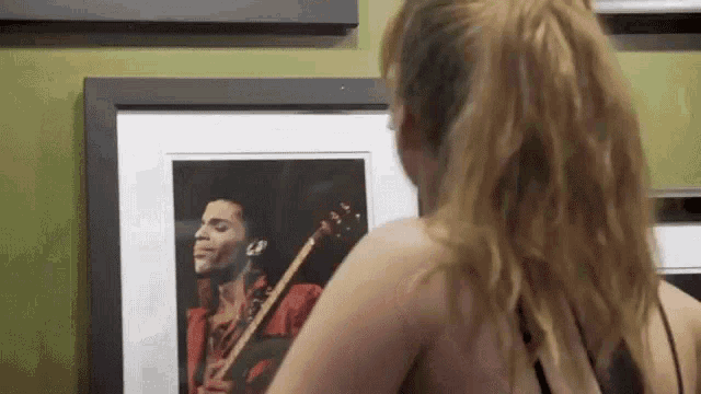 a woman is looking at a picture of prince on a wall .