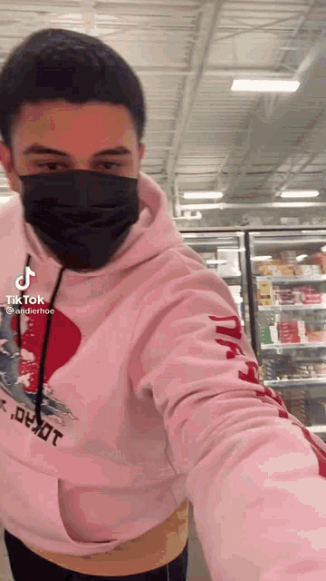 a man wearing a mask and a pink hoodie is standing in a store .