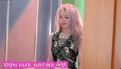 a woman with pink hair is standing in front of a colorful wall and smiling .