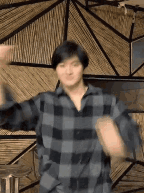 a man in a plaid shirt is dancing in a room with a wooden wall .