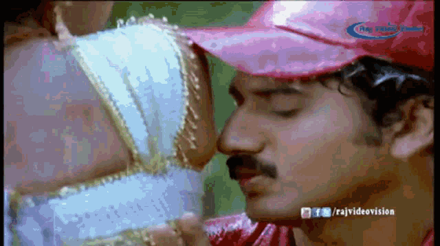 a man in a red hat is kissing a woman 's forehead in a video from raj videovision