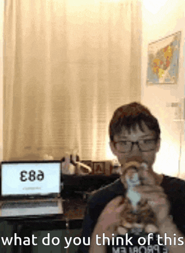 a boy with glasses is drinking a cup of coffee in front of a laptop and a map .