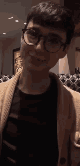 a young man wearing glasses and a tan cardigan is smiling