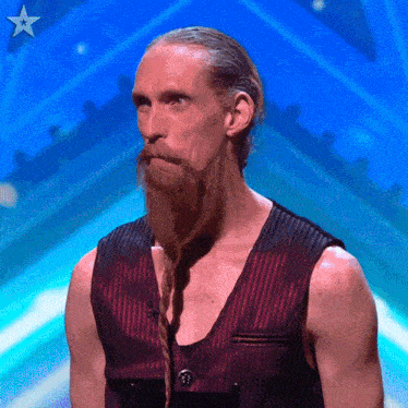 a man with a long beard and braided hair is standing in front of a blue background with a star on it