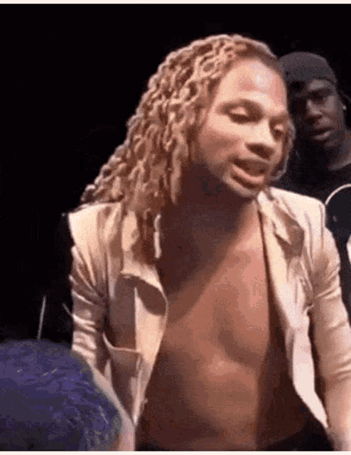 a shirtless man with dreadlocks is standing in a dark room with other people .
