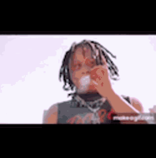 a young man with dreadlocks is blowing a bubble with his hand .