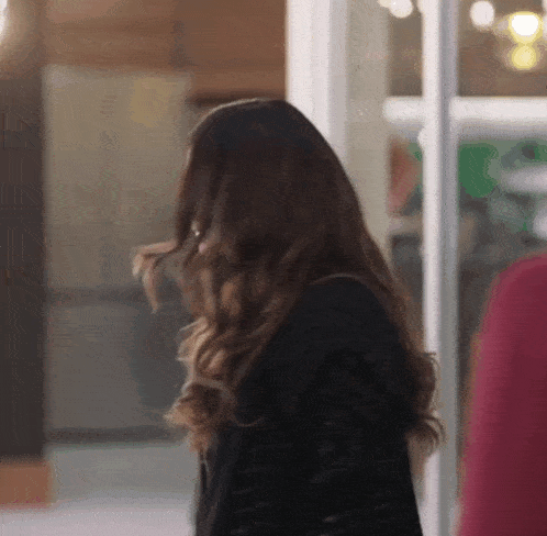 a woman with long hair is standing in front of a glass door and looking over her shoulder .
