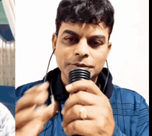 a man in a blue shirt is holding a microphone in front of his face .