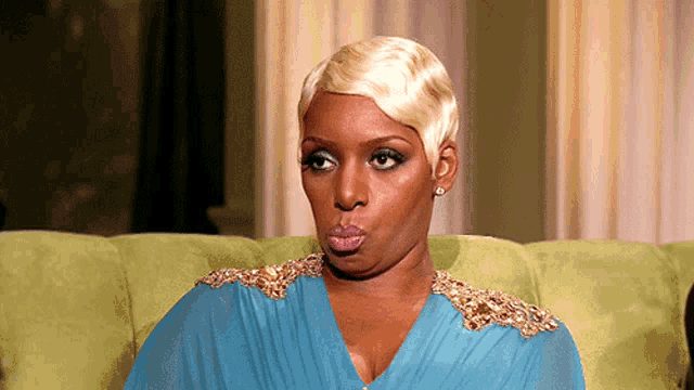 a woman in a blue dress is making a funny face while sitting on a green couch .