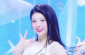a woman in a white tank top with purple hair is smiling in front of a blue background
