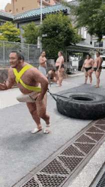 a sumo wrestler is pulling a tire down the street