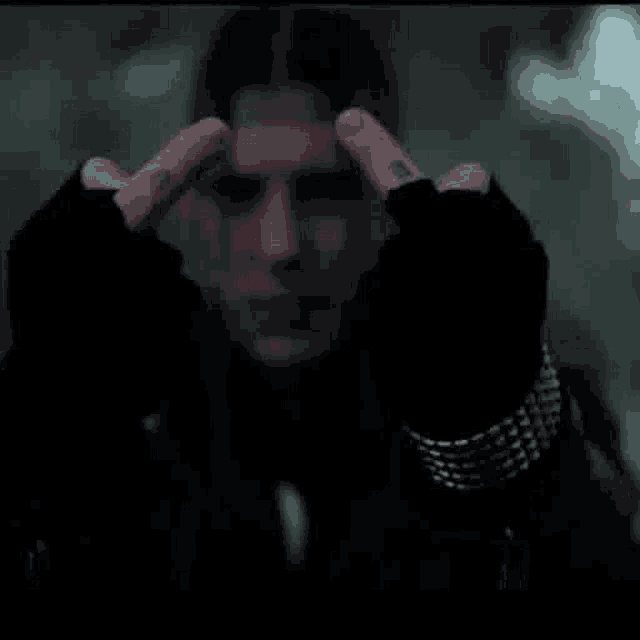 a man with a tattoo on his finger is holding his hands to his forehead .