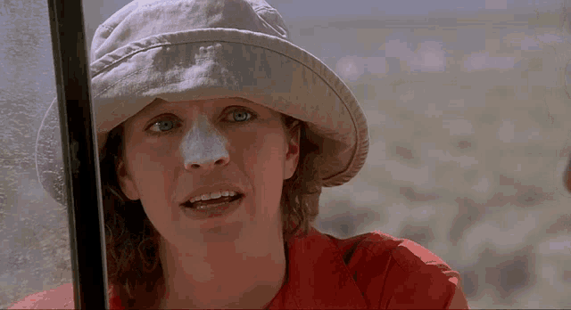 a woman wearing a hat and a red shirt looks at the camera