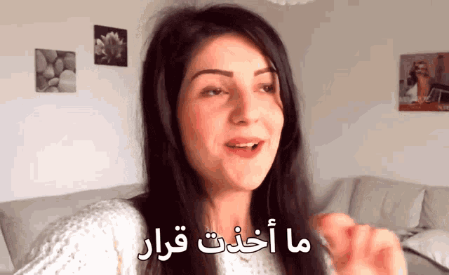 a woman in a white sweater stands in front of a wall with arabic writing on it