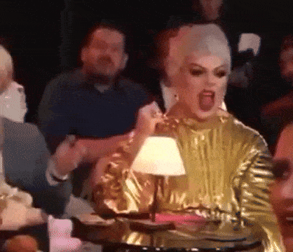 a woman in a gold dress is sitting at a table with a lamp and shouting .