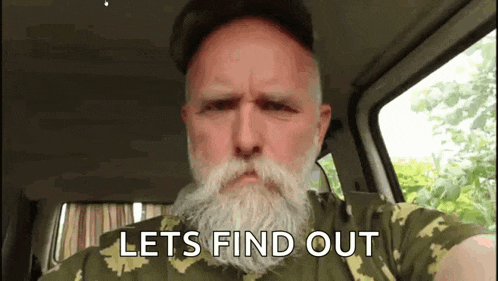 a man with a beard and mustache is sitting in a car with the words `` lets find out '' written on his face .