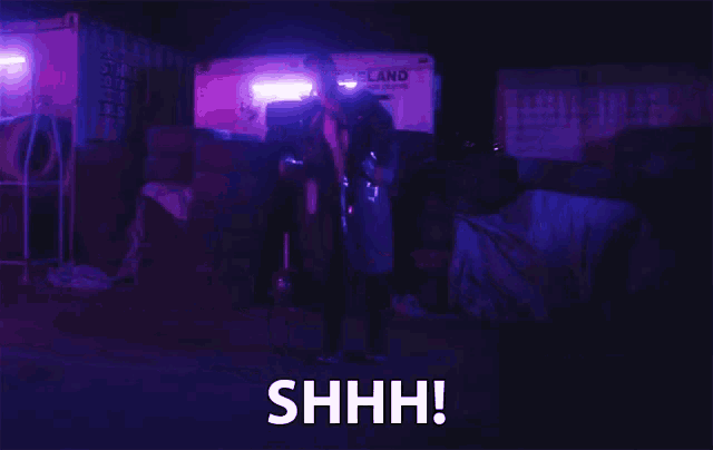a man in a black coat says shhh in front of a white truck